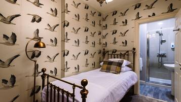 A bedroom with a bed, a nightstand, a lamp, and a shower area.