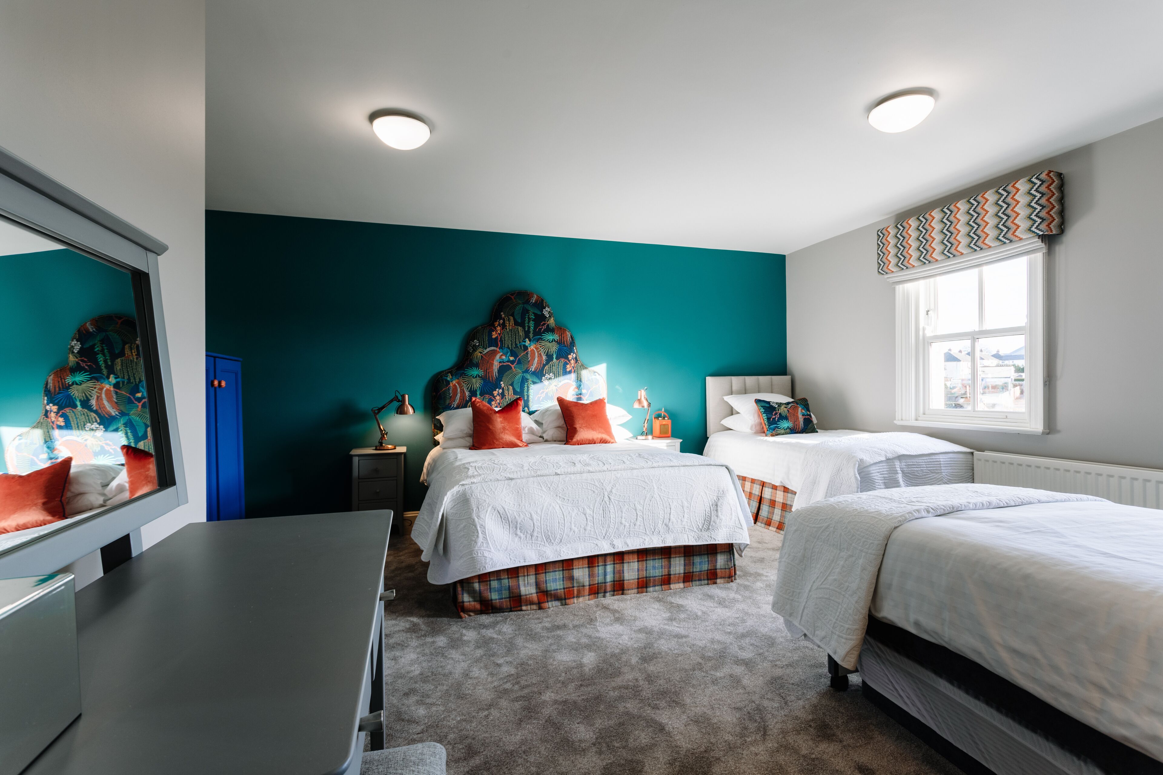 A bedroom with two beds, teal walls, and a large mirror.