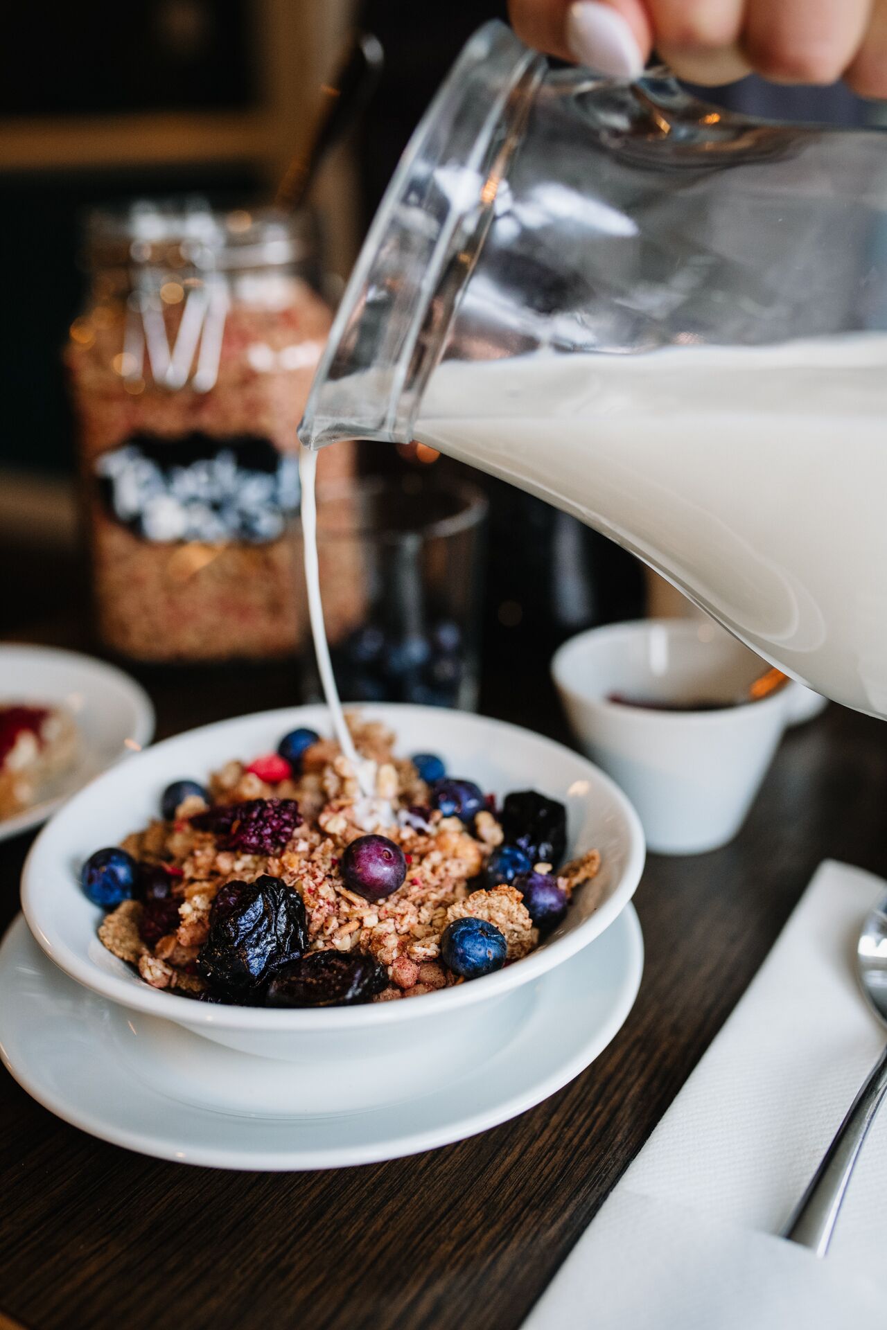 A bowl of cereal with blueberries and granola being topped with milk.