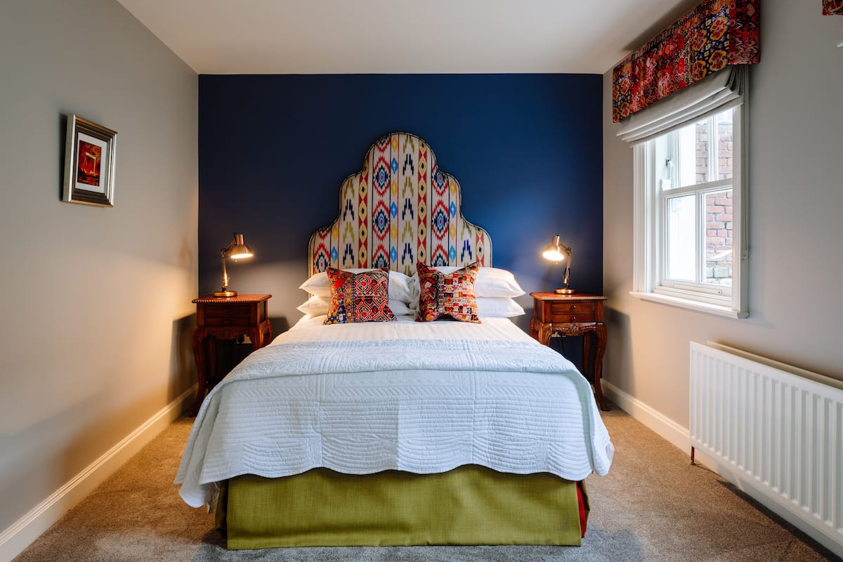 A neatly arranged bedroom with a large bed, two bedside tables with lamps, a window with a view, and a framed picture on the wall.