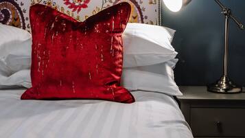 A bed with white linens, a red decorative pillow, and a bedside lamp.