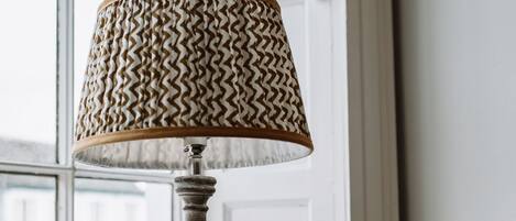 Una lámpara de mesa con pantalla estampada sobre una mesa de madera cerca de una ventana.