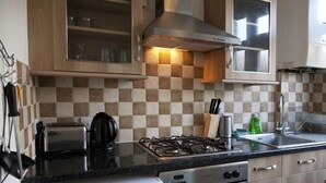 A kitchen with a gas stove, oven, and microwave. There are wooden cabinets and a checkered backsplash. - Tooting Place Apartments (Mitcham)