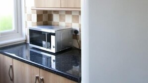 A kitchen with a microwave on a black countertop, wooden cabinets, and a window. - Tooting Place Apartments (Mitcham)