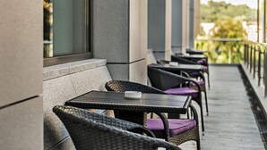 A row of outdoor wicker chairs with cushions, aligned along a balcony with a view of greenery in the background.