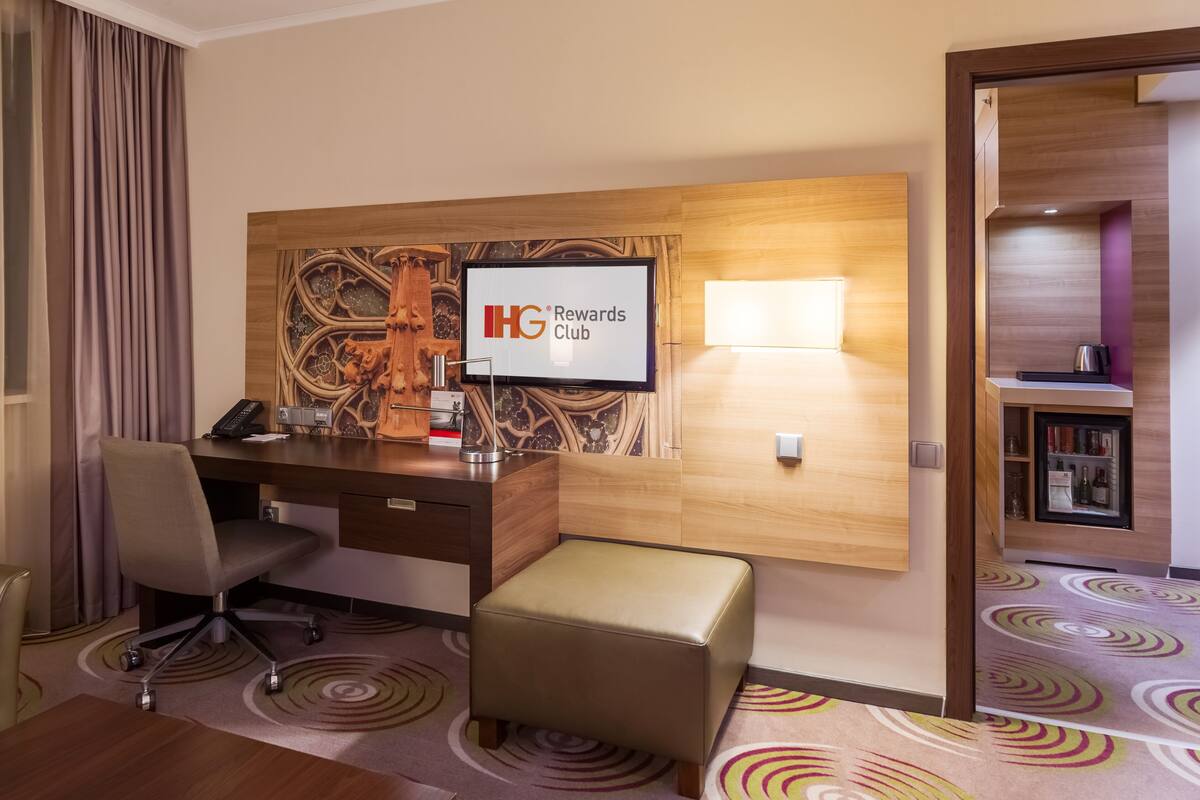A hotel room with a desk, chair, and a television displaying "IHG Rewards Club".