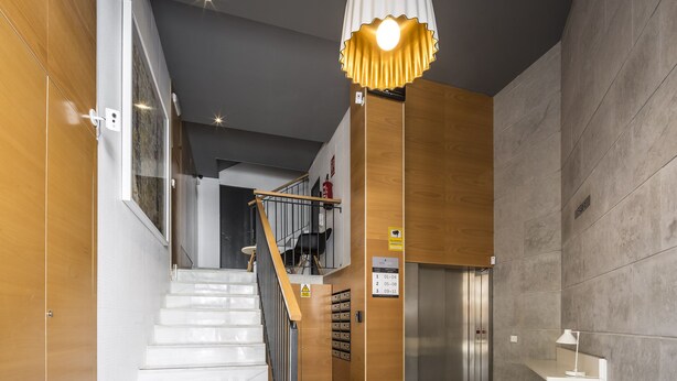 Un interior moderno con una escalera, paneles de madera y una lámpara colgante.