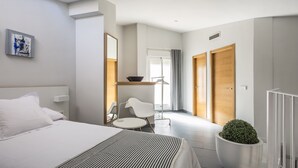 Habitación de hotel moderna con cama, un pequeño escritorio, una silla, una planta en maceta y vistas al pasillo.