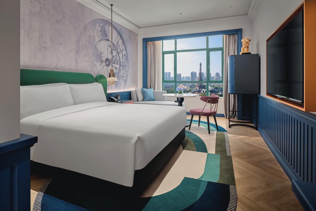 Ein Hotelzimmer mit einem großen Bett, einer Couch, einem Fernseher und Blick auf eine Stadtansicht durch das Fenster.