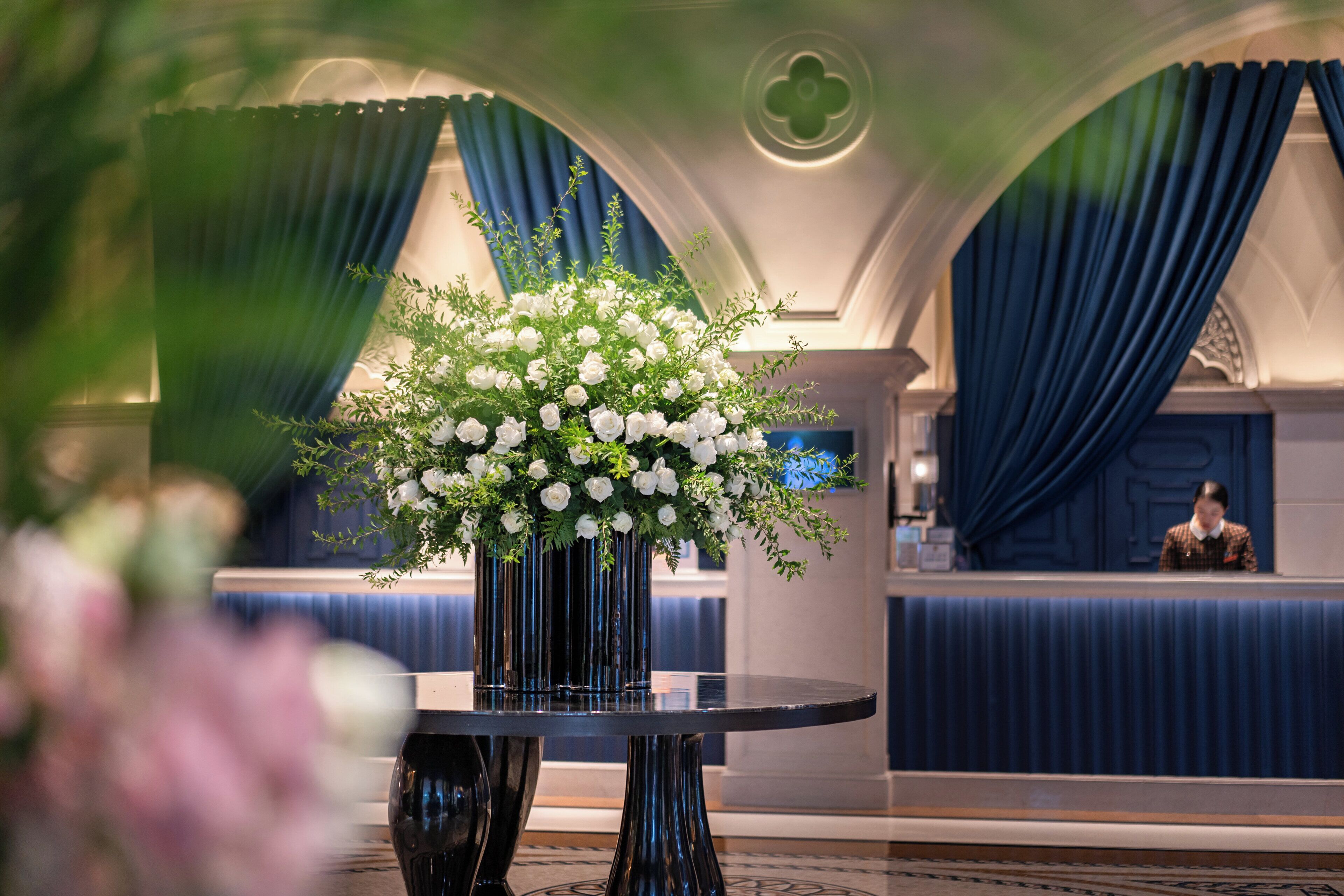 A reception area with a black table, a floral centerpiece, and blue drapes.
