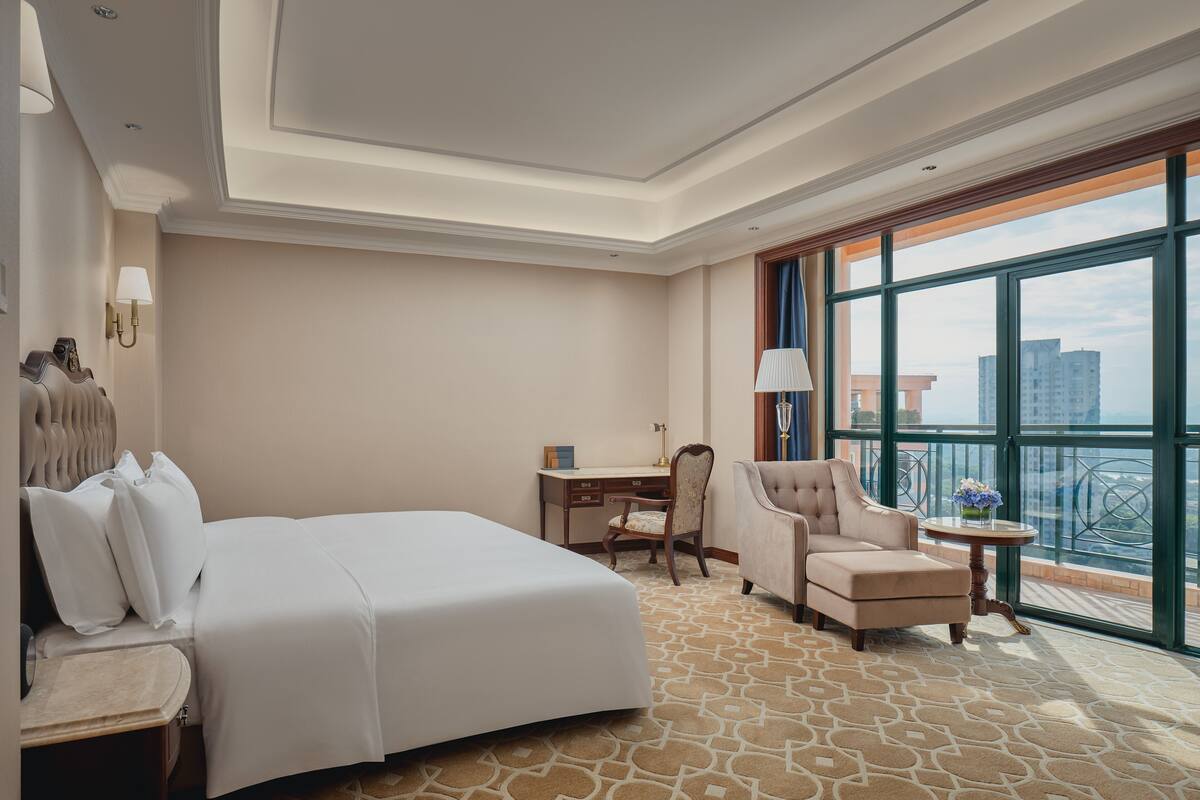 Ein Hotelzimmer mit einem großen Bett, einem Schreibtisch, einem Stuhl und einem Balkon mit Blick auf die Stadt.