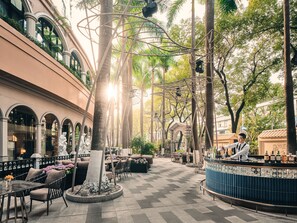 Un espacio al aire libre con mesas, sillas, una barra y un árbol decorativo.