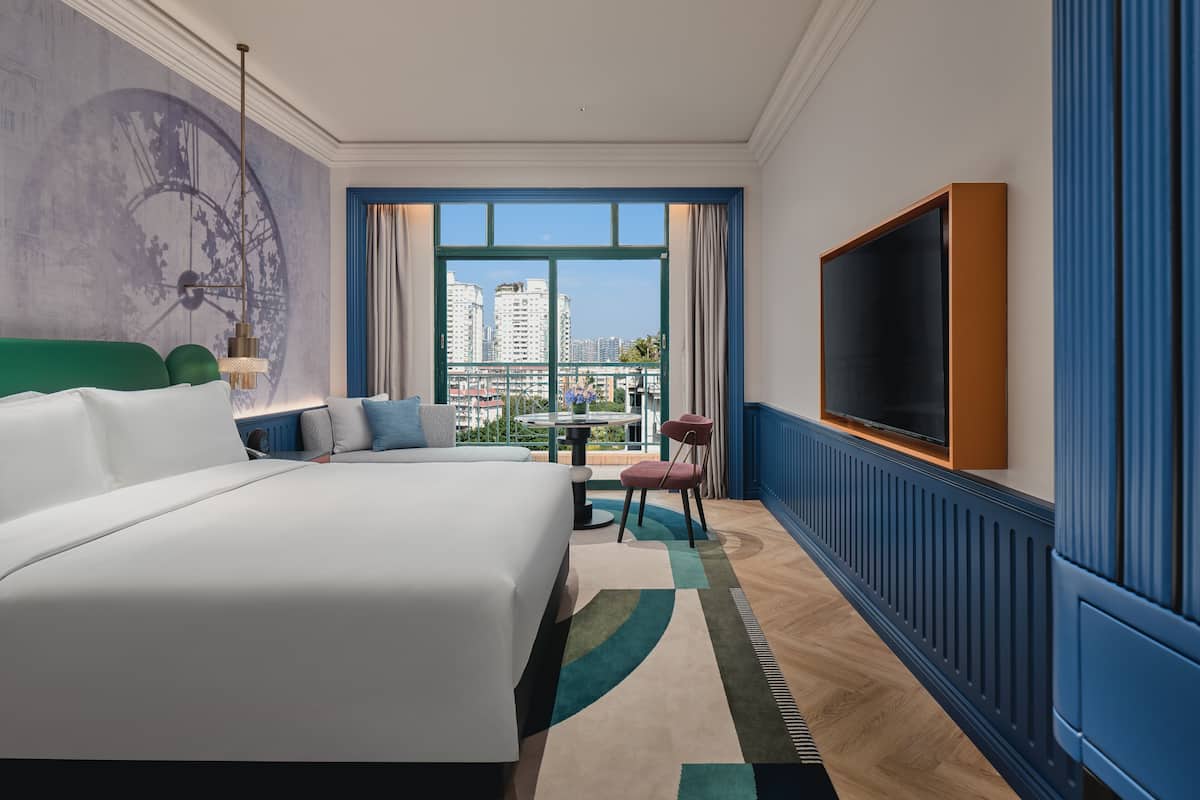 Ein Hotelzimmer mit einem großen Bett, einem Fernseher, Blick auf die Stadt und einem Balkon.