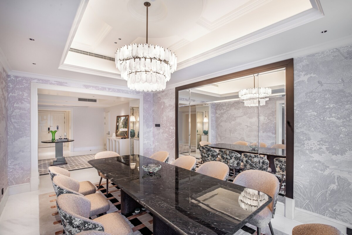 Uma sala de jantar moderna com uma mesa de mármore, cadeiras estofadas e um espelho grande.