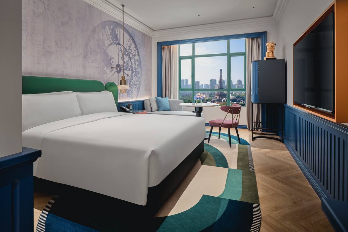 Ein modernes Hotelzimmer mit einem großen Bett, einer Couch, einem Fernseher und Blick auf die Stadt.