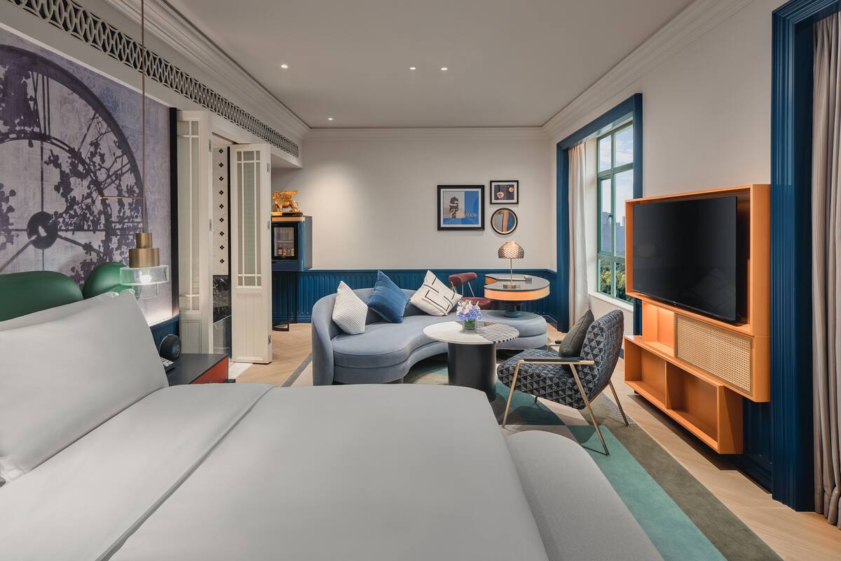 Ein modernes Hotelzimmer mit einem großen Bett, einer Sitzecke mit rundem Tisch, einem Fernseher und einem dekorativen Wandbild.
