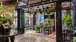 Un lobby lujoso con piso de diseño a cuadros, barandillas de metal negro ornamentadas y varias plantas en macetas.