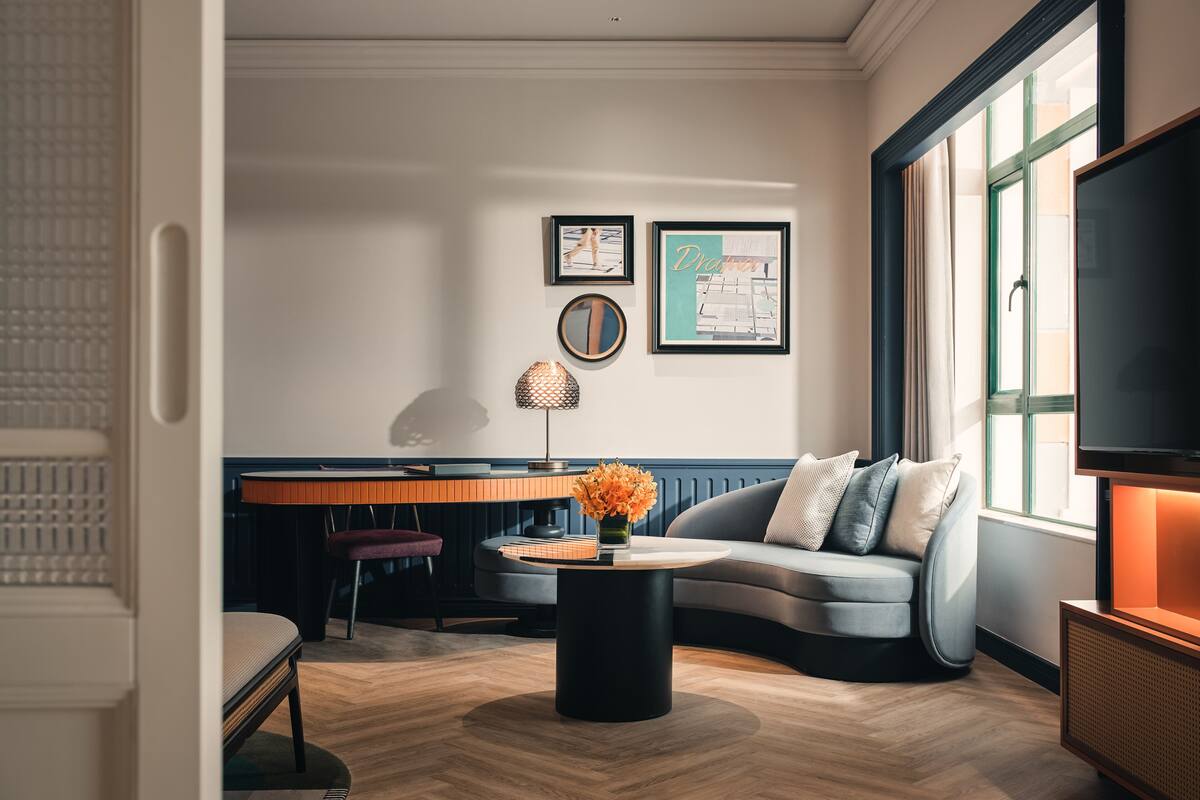 Ein modernes Wohnzimmer mit einer Couch, einem Couchtisch und einem Fernseher. An der Wand hängen gerahmte Bilder und es gibt ein Fenster mit Vorhängen.