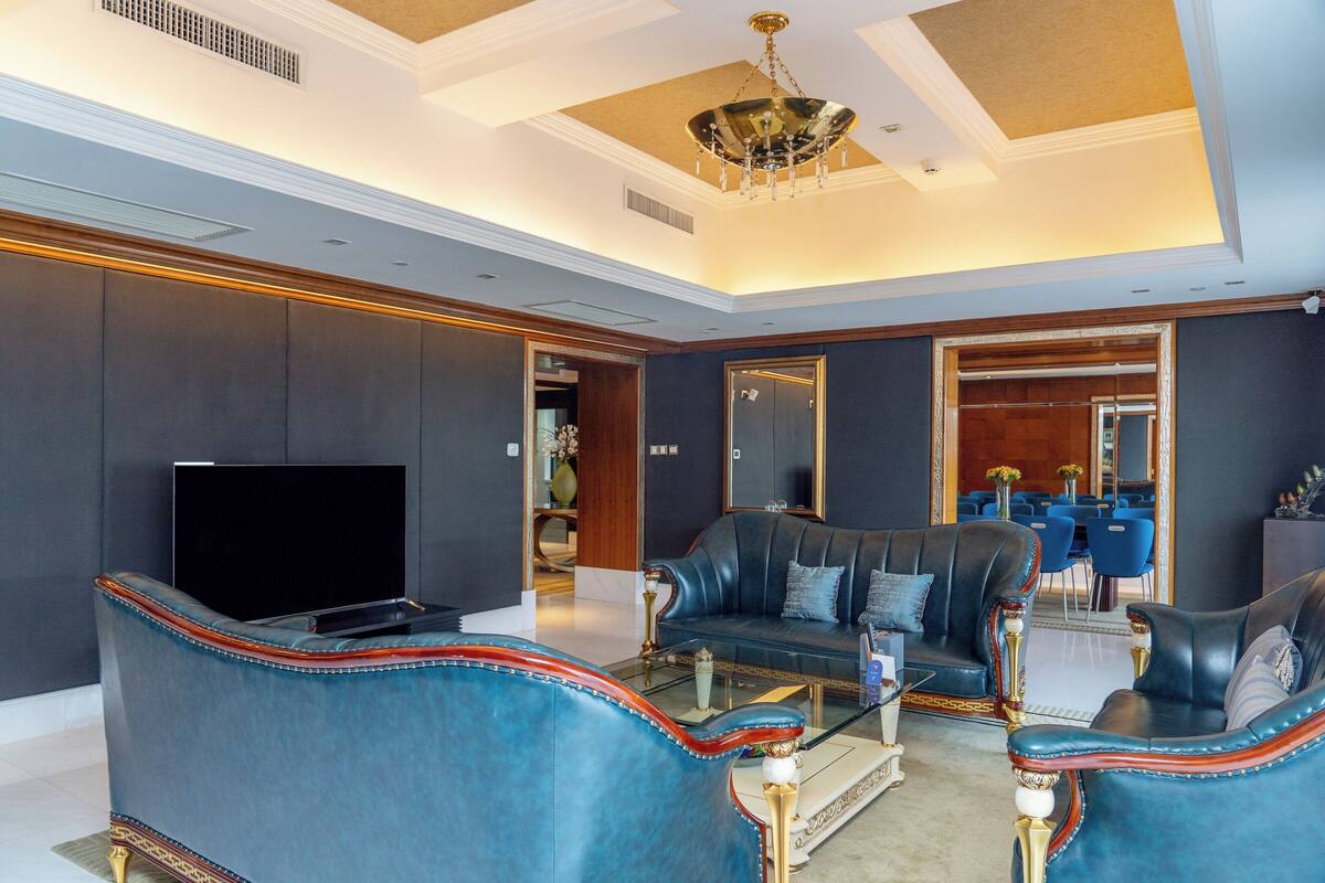 Ein luxuriöses Wohnzimmer mit großem Flachbildfernseher, Ledersofas, einem Glastisch und einer Kristallleuchter.