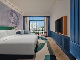 A hotel room with a large bed, a television, a view of the city, and a balcony.