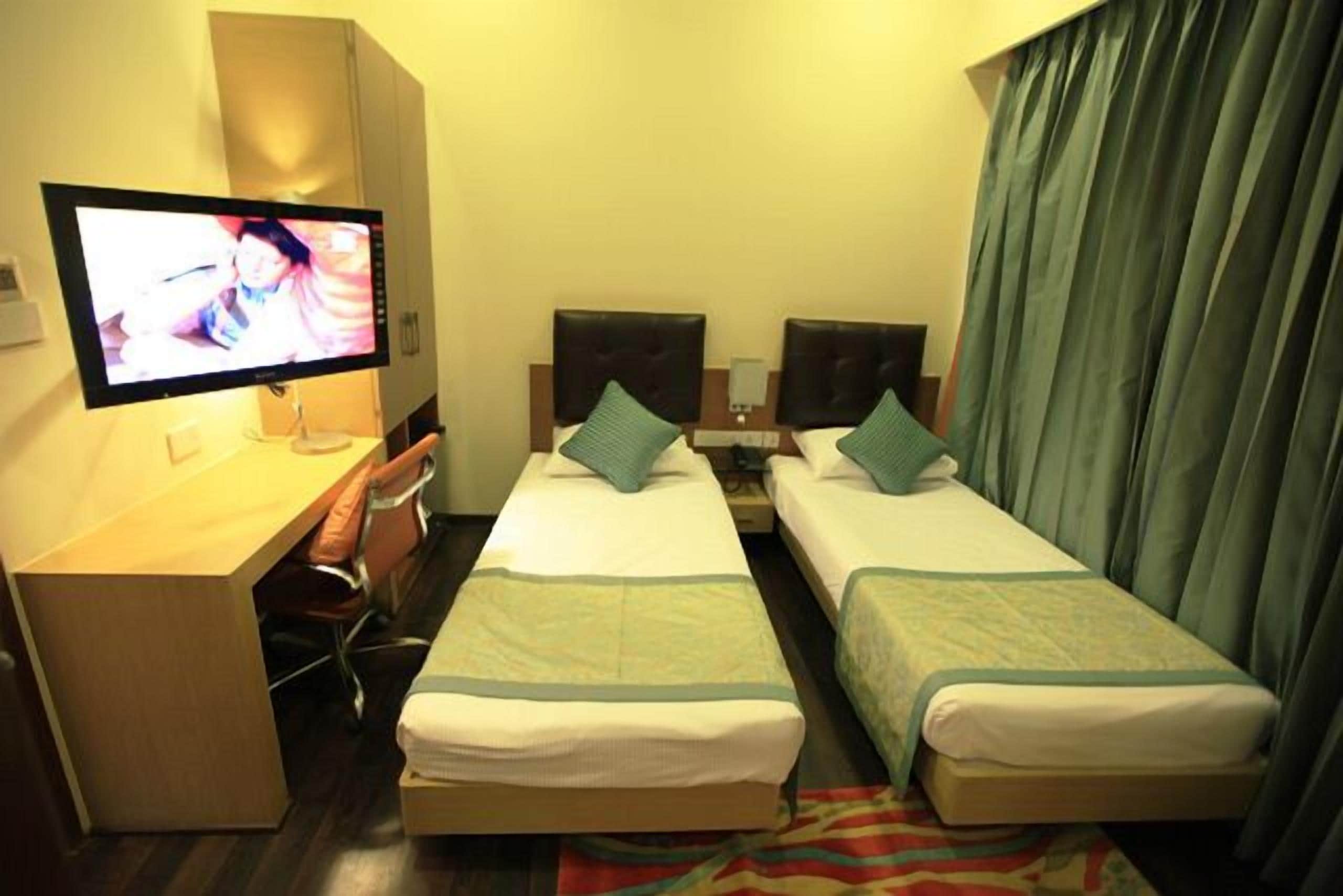 A hotel room with two single beds, a desk with a computer, and a TV.
