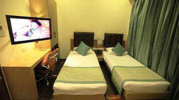 A hotel room with two single beds, a desk with a computer, and a TV.