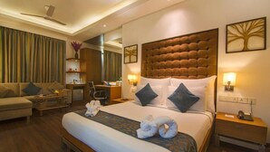 A hotel room with a large bed, a sofa, a desk, and a chair. - Riverview Hotel (Ahmedabad)