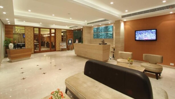 A modern hotel lobby with a reception desk, seating area, and a television mounted on the wall. - Riverview Hotel (Ahmedabad)