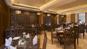 A restaurant with wooden decor, multiple tables set with white tablecloths, and hanging light fixtures. - Riverview Hotel (Ahmedabad)