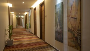 A hotel hallway with patterned carpet, wooden doors, and artwork on the walls. - Riverview Hotel (Ahmedabad)