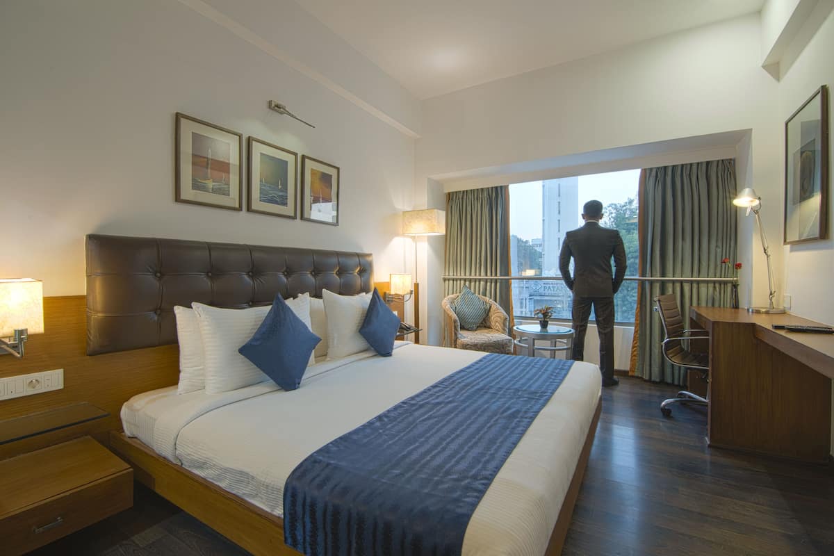 Quarto de hotel com uma cama grande, uma escrivaninha, uma cadeira e vista para a cidade pela janela.