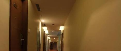 A hotel hallway with a patterned carpet, doors on both sides, and overhead lighting.