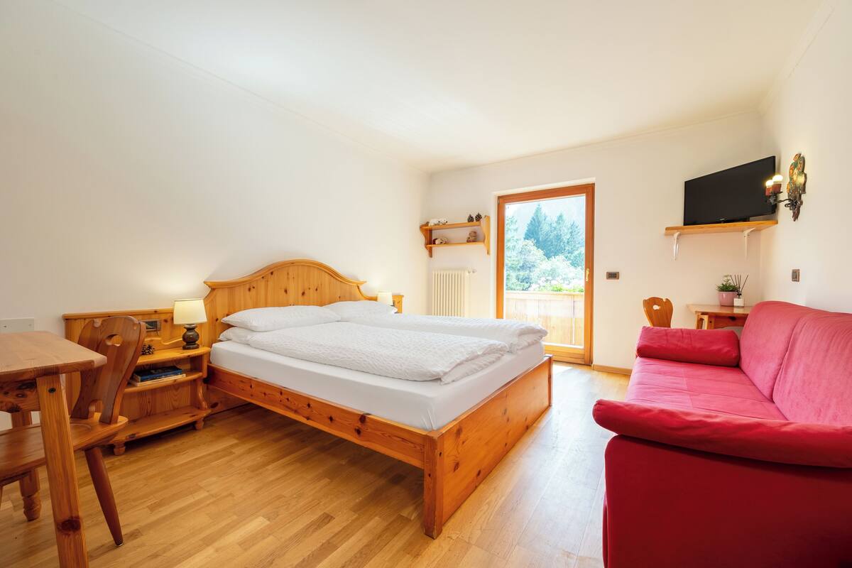 Een slaapkamer met een houten bed, een rode bank, een houten bureau en een televisie aan de muur.