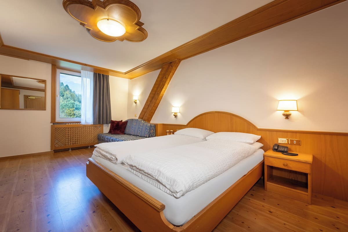 Hotelkamer met een groot bed, houten hoofdeinde, bedlampen, een nachtkastje en een raam met uitzicht op groen.