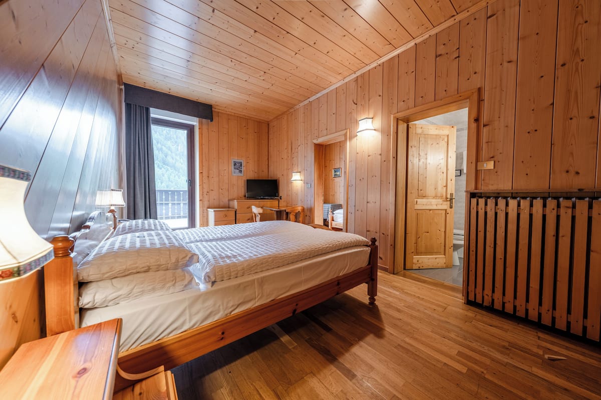 Een slaapkamer in een houten hutje, met een bed, nachtkastje, lamp en een televisie.