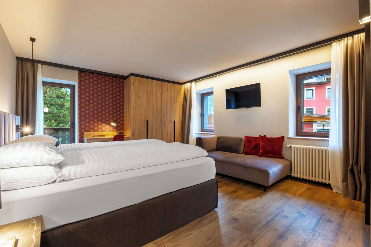 Een moderne slaapkamer met een groot bed, een sofa, een aan de muur bevestigde televisie en een raam met gordijnen.