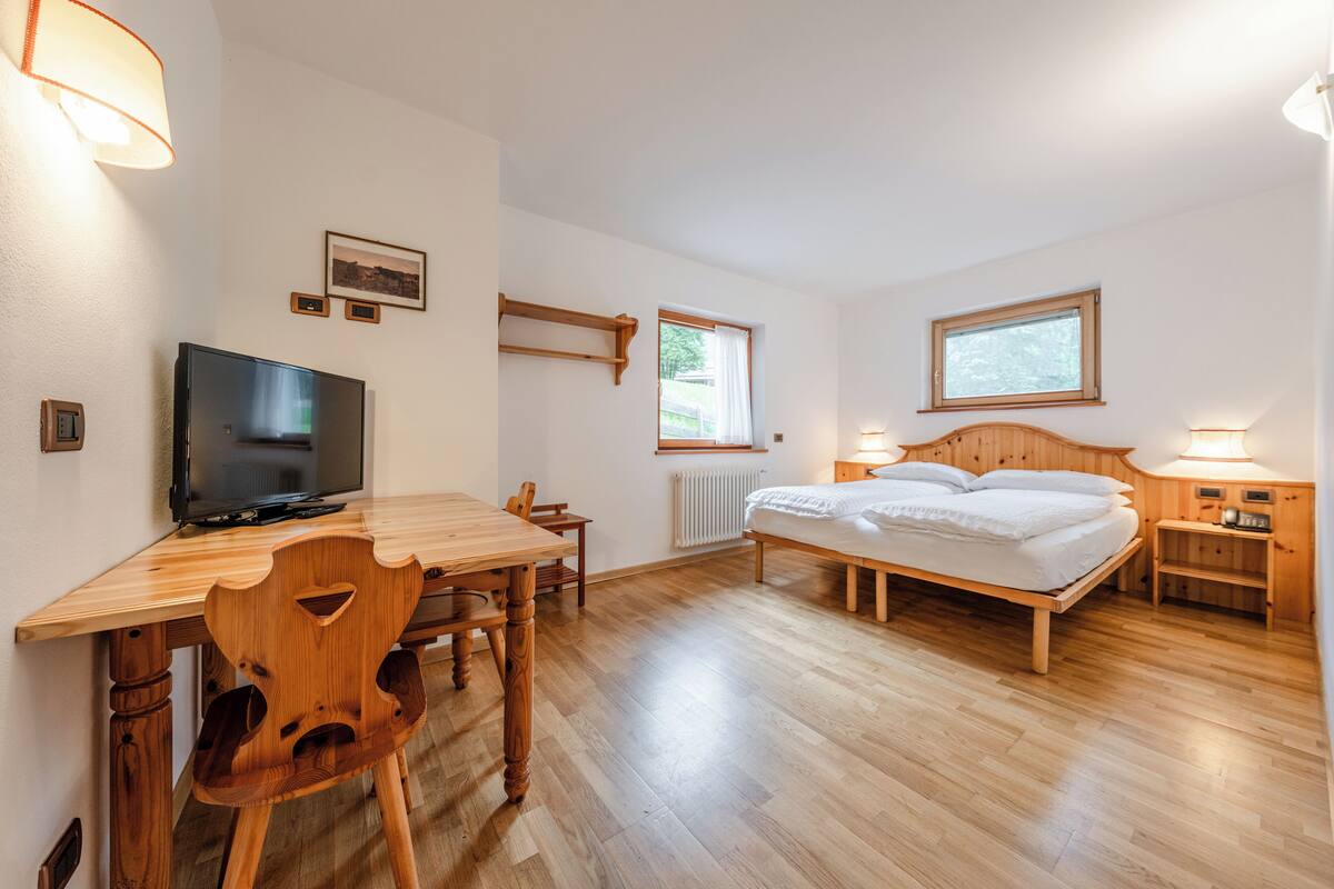 Een slaapkamer met een houten bed, een bureau met een televisie en een stoel.