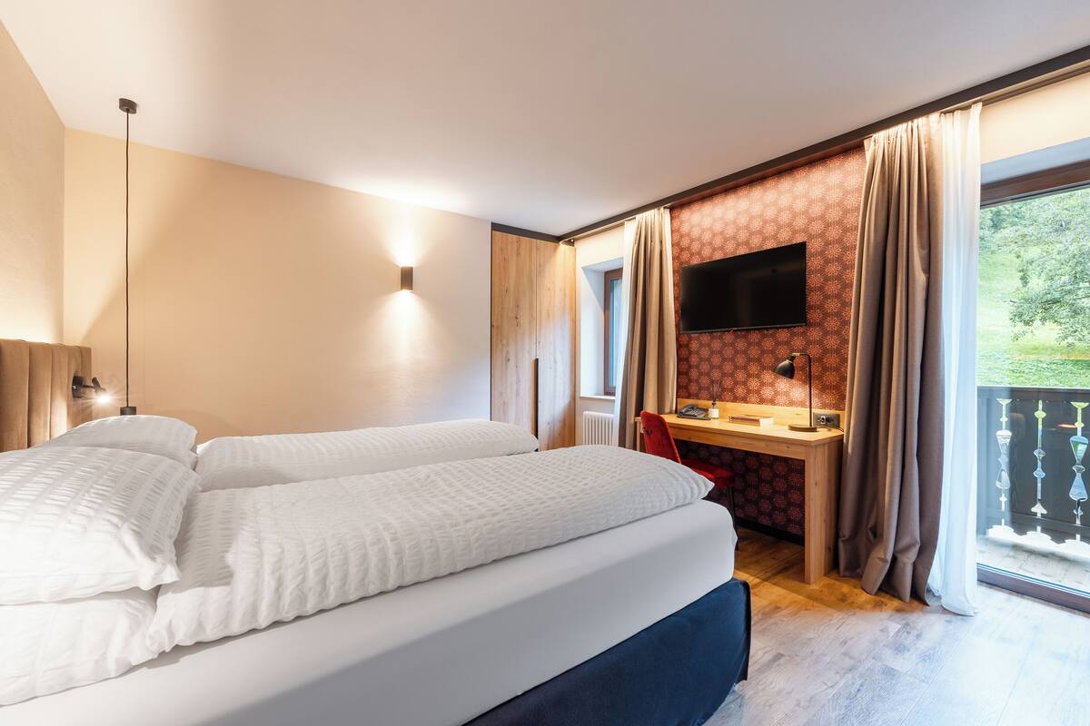 Hotelkamer met een groot bed, een bureau met een computer, een televisie en een balkon met gordijnen.