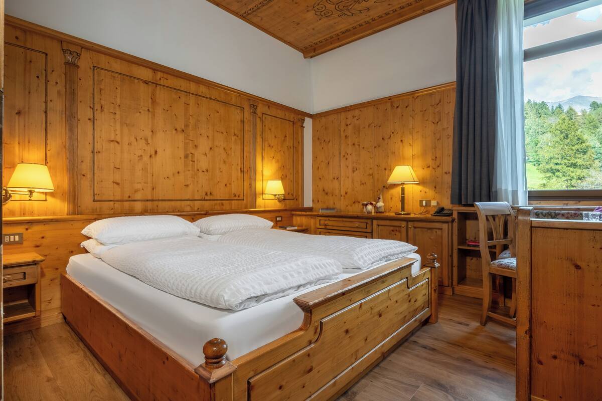 Een houten slaapkamer met een groot bed, twee bedlampen, een bureau en een stoel.