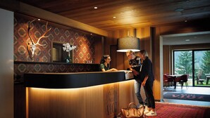 Ein Hotelrezeptionstresen mit ornamentalem Wandpapier, einer großen Lampe und einer Holzzieldecke.