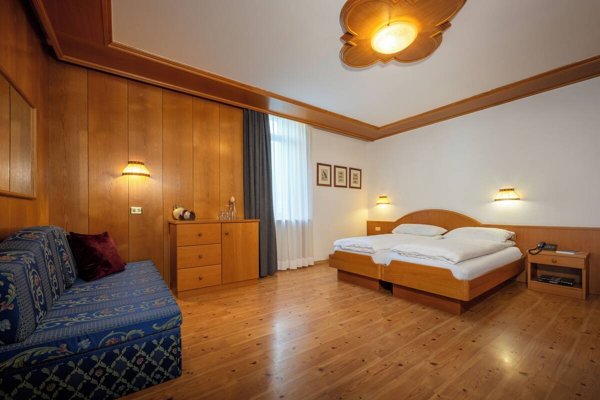 Een hotelkamer met een houten bed, een bank, een nachtkastje en een wandlamp.