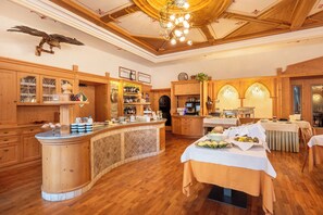 A spacious kitchen with wooden cabinets, a central island, and a dining area with tables set for a meal. - Hotel Vioz - Family Hotel & Apartments (Pejo)