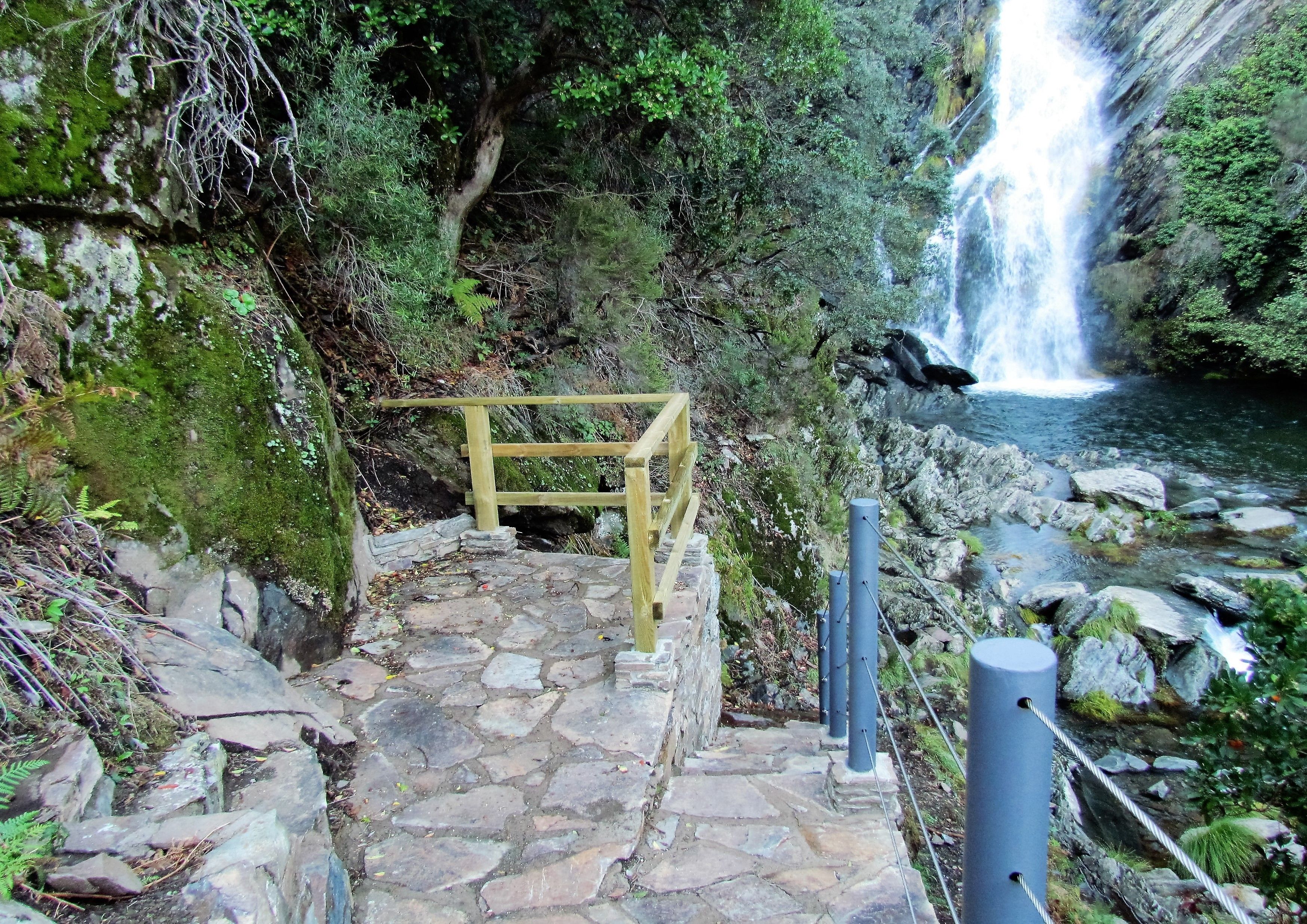 A stone staircase leading to a wooden viewing platform overlooking a waterfall.