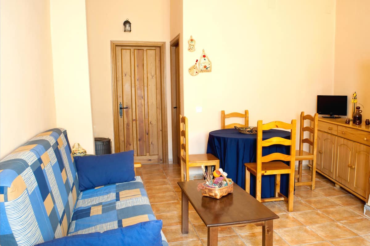 Una sala de estar con sofá, una mesa, una mesa de comedor con sillas, un televisor y una puerta de madera.