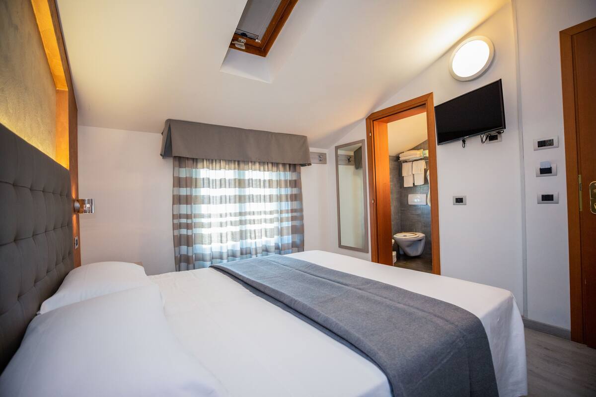 A hotel room with a bed, a television mounted on the wall, and a bathroom visible through an open door.