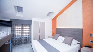 Una habitación de hotel moderna con una cama grande, una cama litera, un armario y una mesita.