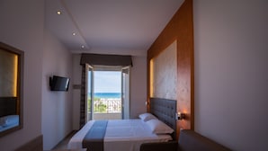 Une chambre d’hôtel équipée d’un lit, d’un bureau, d’une chaise, d’une télévision et d’un balcon avec vue sur la plage.
