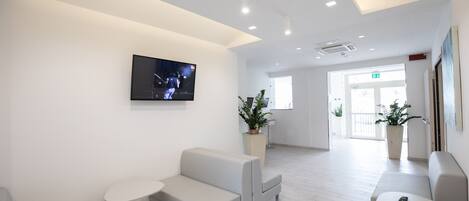 Una recepción moderna y bien iluminada, con una televisión de pantalla plana, asientos y plantas en macetas.
