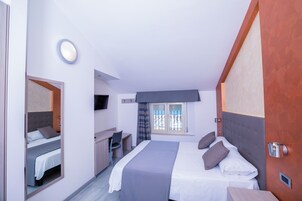 Camera d'albergo moderna con un letto grande, una scrivania, una sedia, una TV e una finestra con tende.