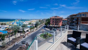 Une vue sur la côte depuis un balcon, avec un ciel dégagé, une route où circulent des véhicules et, au loin, une plage.